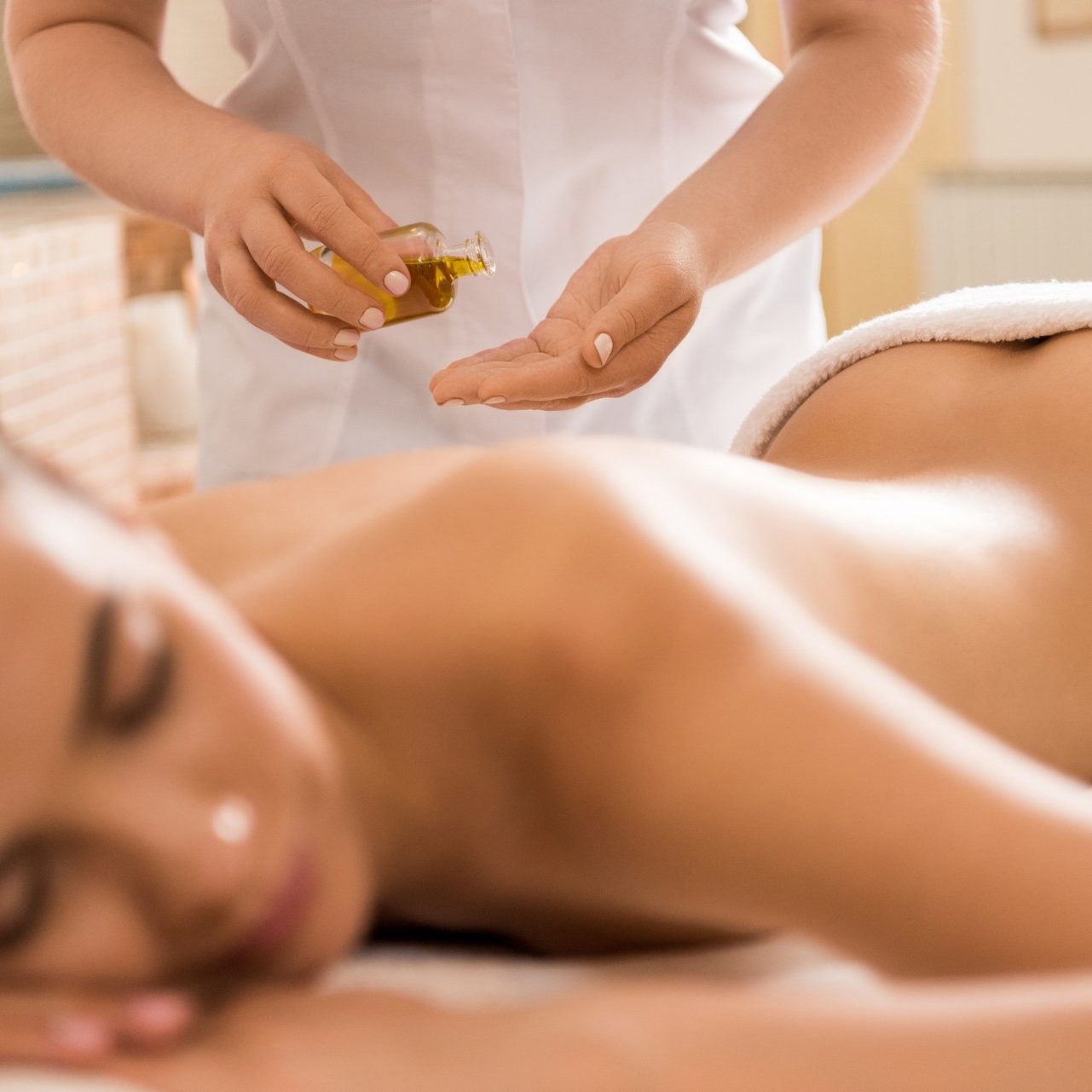 massage therapist making massage with body oil for woman in spa salon